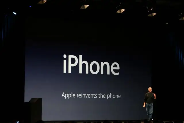 Steve Jobs op het podium bij de presentatie van de iPhone in 2007. Op het scherm staat "Apple reinvents the phone"